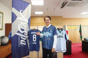 アビスパ福岡から提供いただいたシャツを着用し、紺野選手のユニフォームとともに写る安川町長