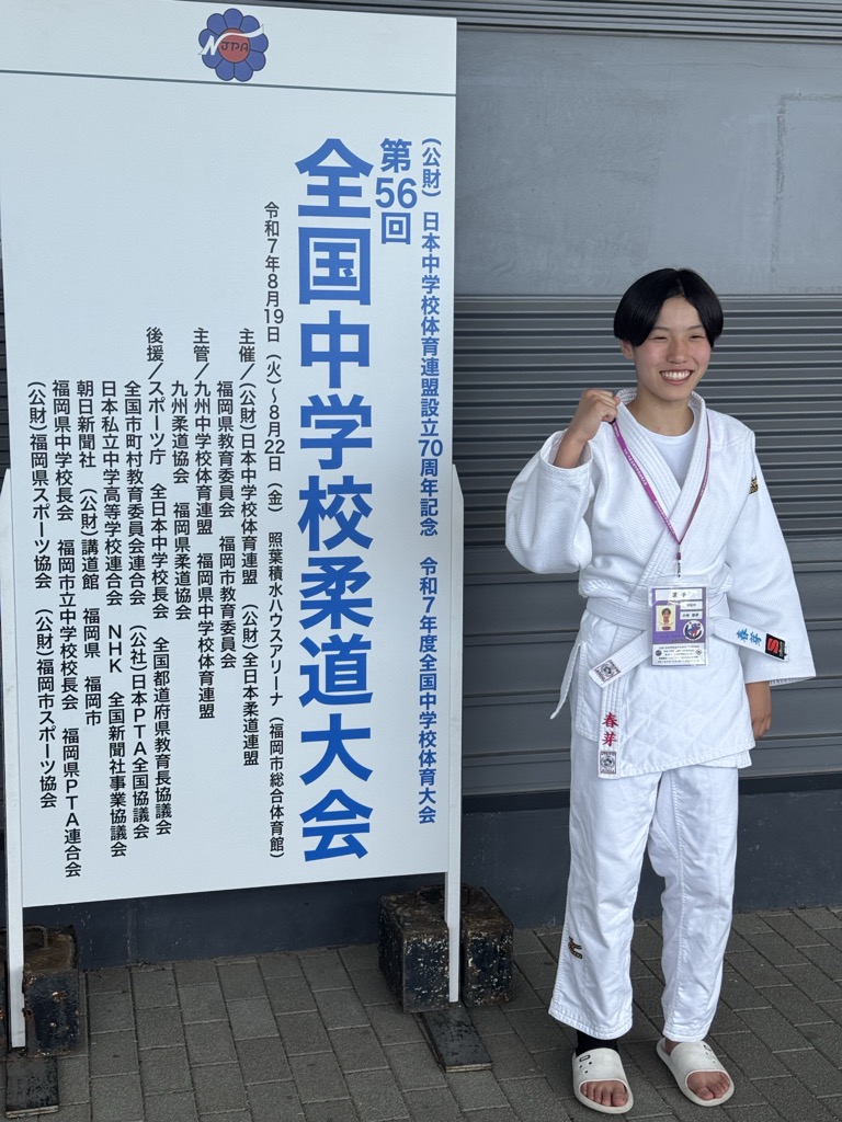 大会記念看板前でガッツポーズをする小林春芽さんの写真
