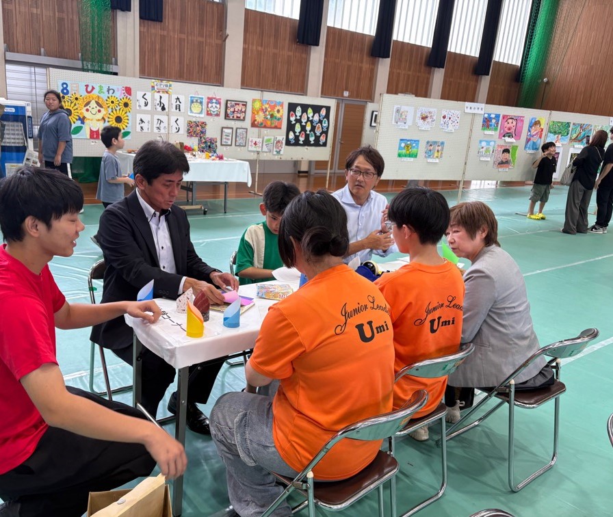 宇美町リーダー会の中高生たちに火の玉飛行機の折り方を習う安川町長