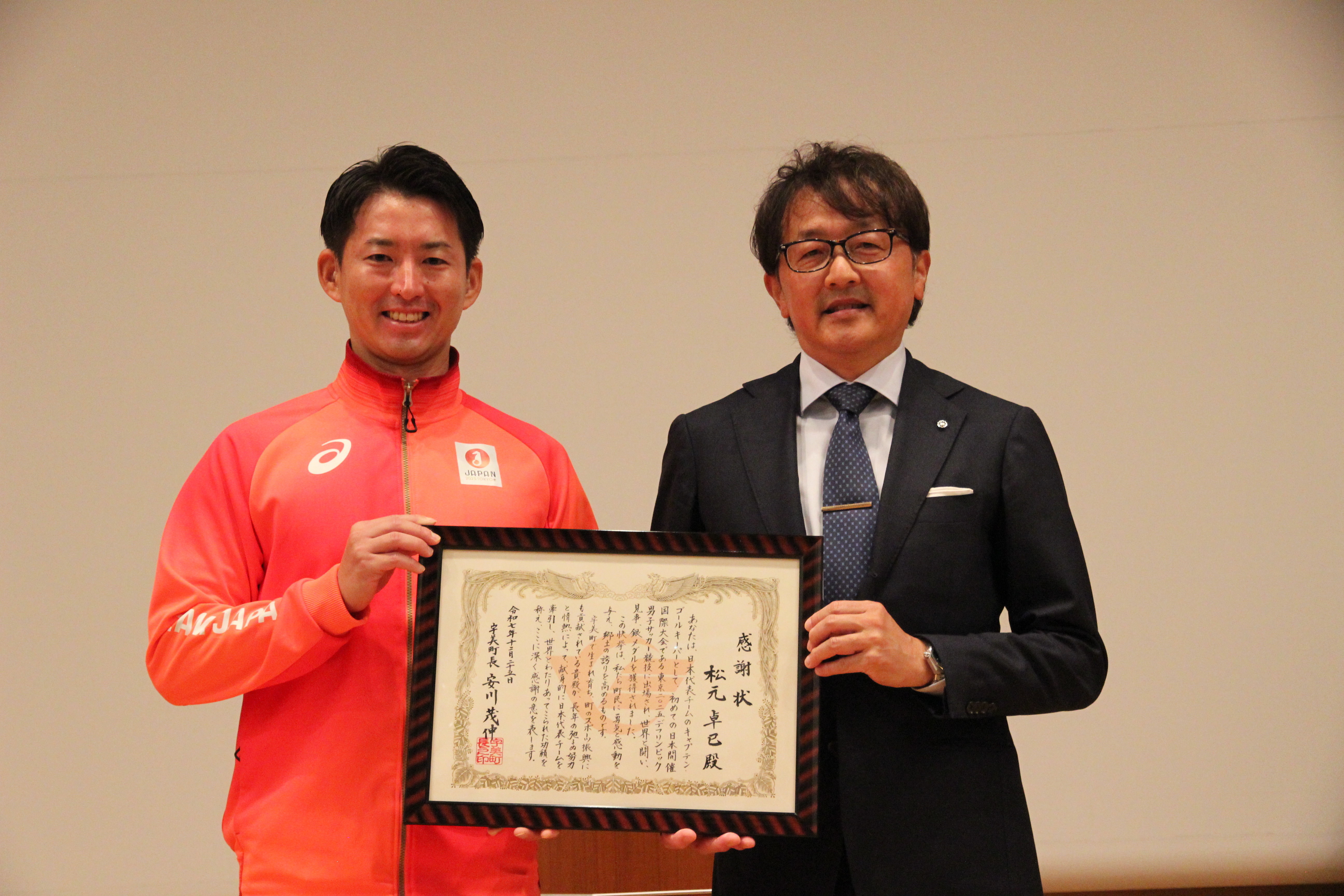 宇美町から松元選手へ授与された感謝状を持って町長と松元選手が記念撮影